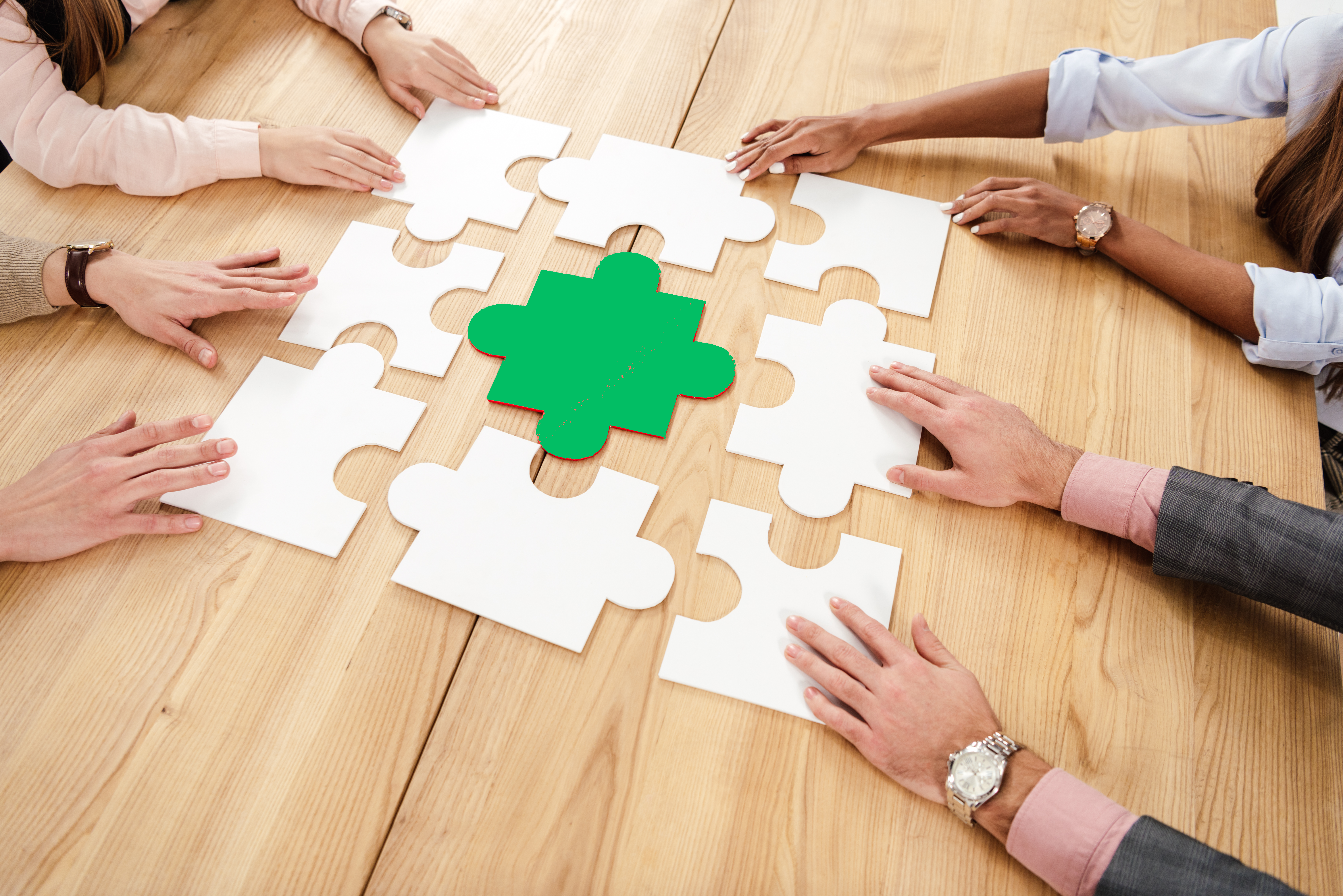 Multiracial team collaboratively assembling a jigsaw puzzle on a wooden table, symbolizing teamwork and problem-solving