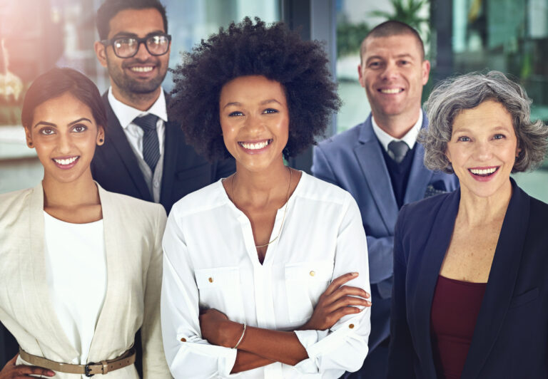 A diverse group of professionals smiling confidently, including two women and three men of various ages and ethnic backgrounds, representing teamwork and success in a modern business environment.